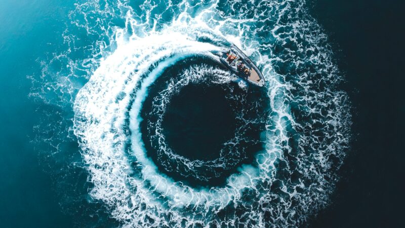 A motorboat photographed from the air traces a perfect circle on the surface of a dark sea.